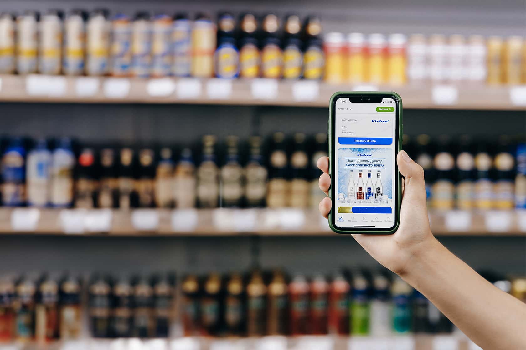 A customer with a phone choosing drinks from the shelves of a Volna store