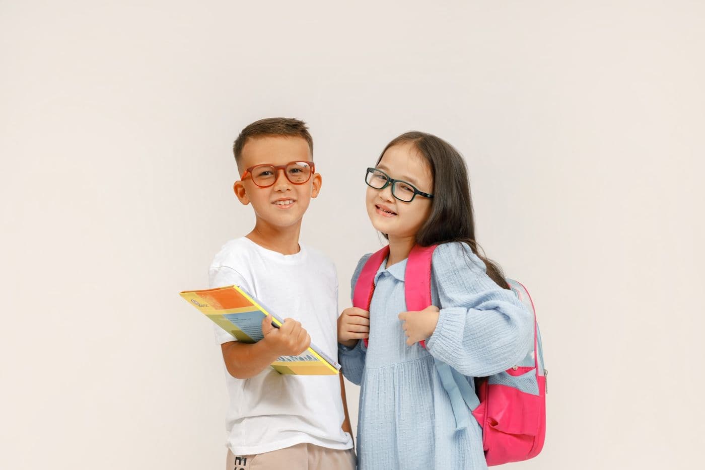A boy and a girl in glasses with a book and a pink backpack