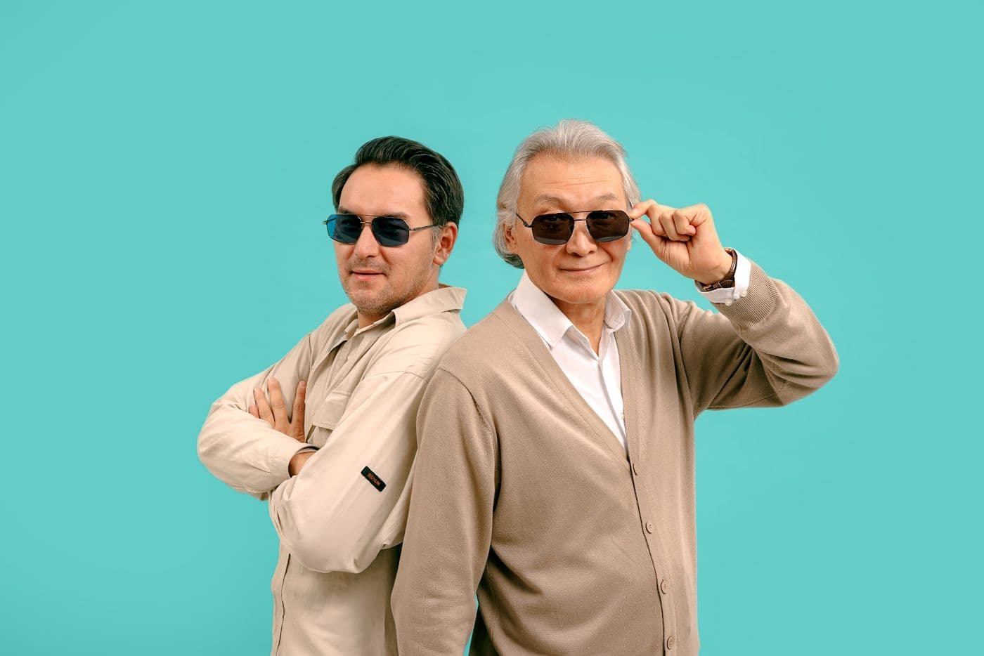 Two men in sunglasses on a turquoise background, the older one holding the frame