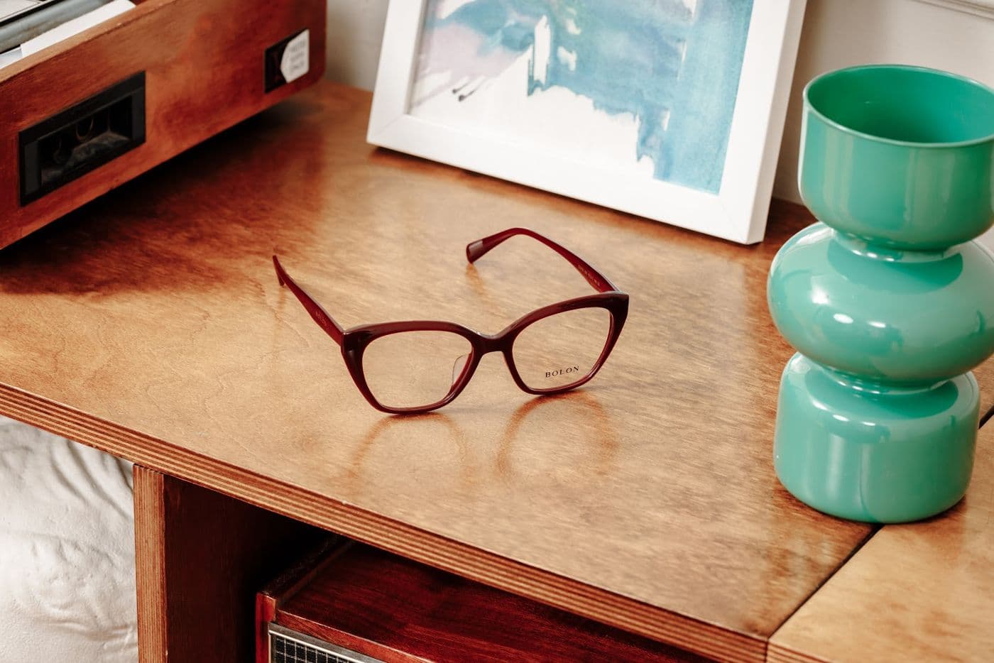 Glasses with a red frame on a wooden cabinet next to a vase
