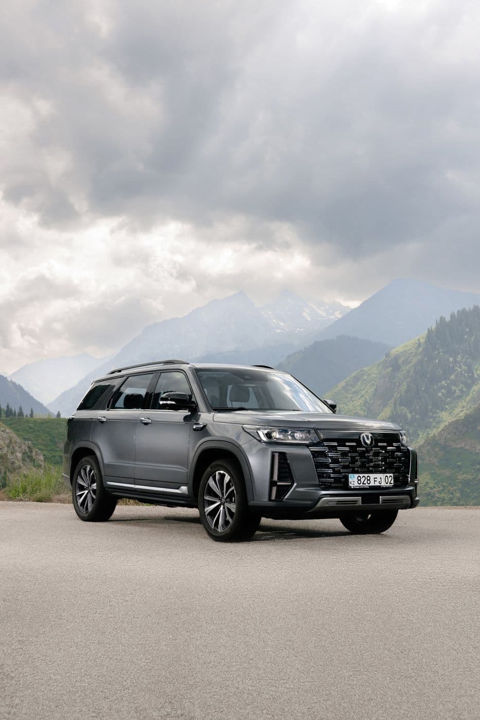 Серый внедорожник Changan на горной дороге на фоне облаков и гор