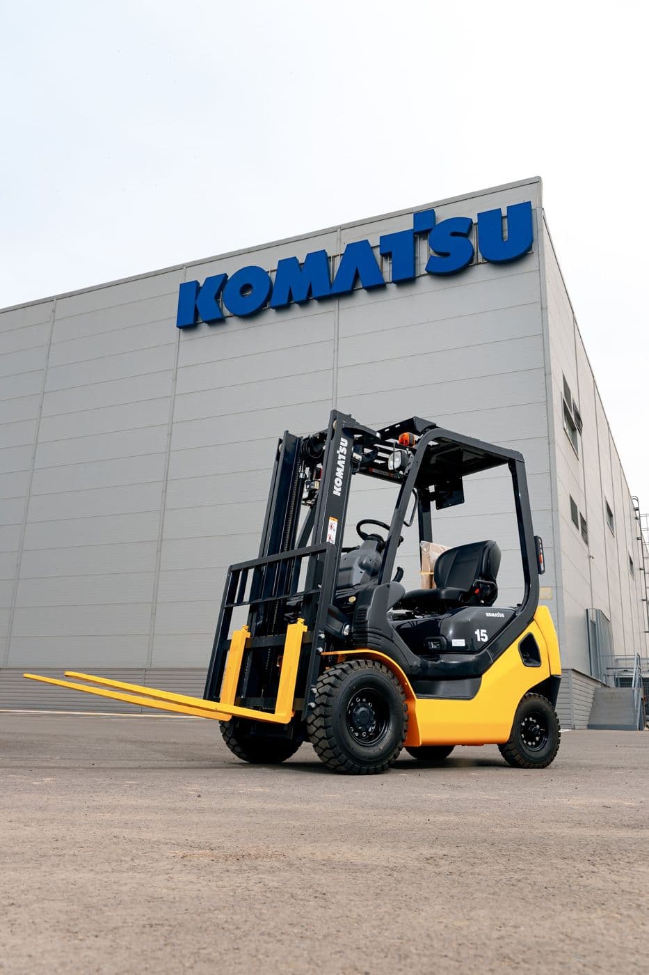 Жёлтый вилочный погрузчик Komatsu на площадке перед складом с синим логотипом