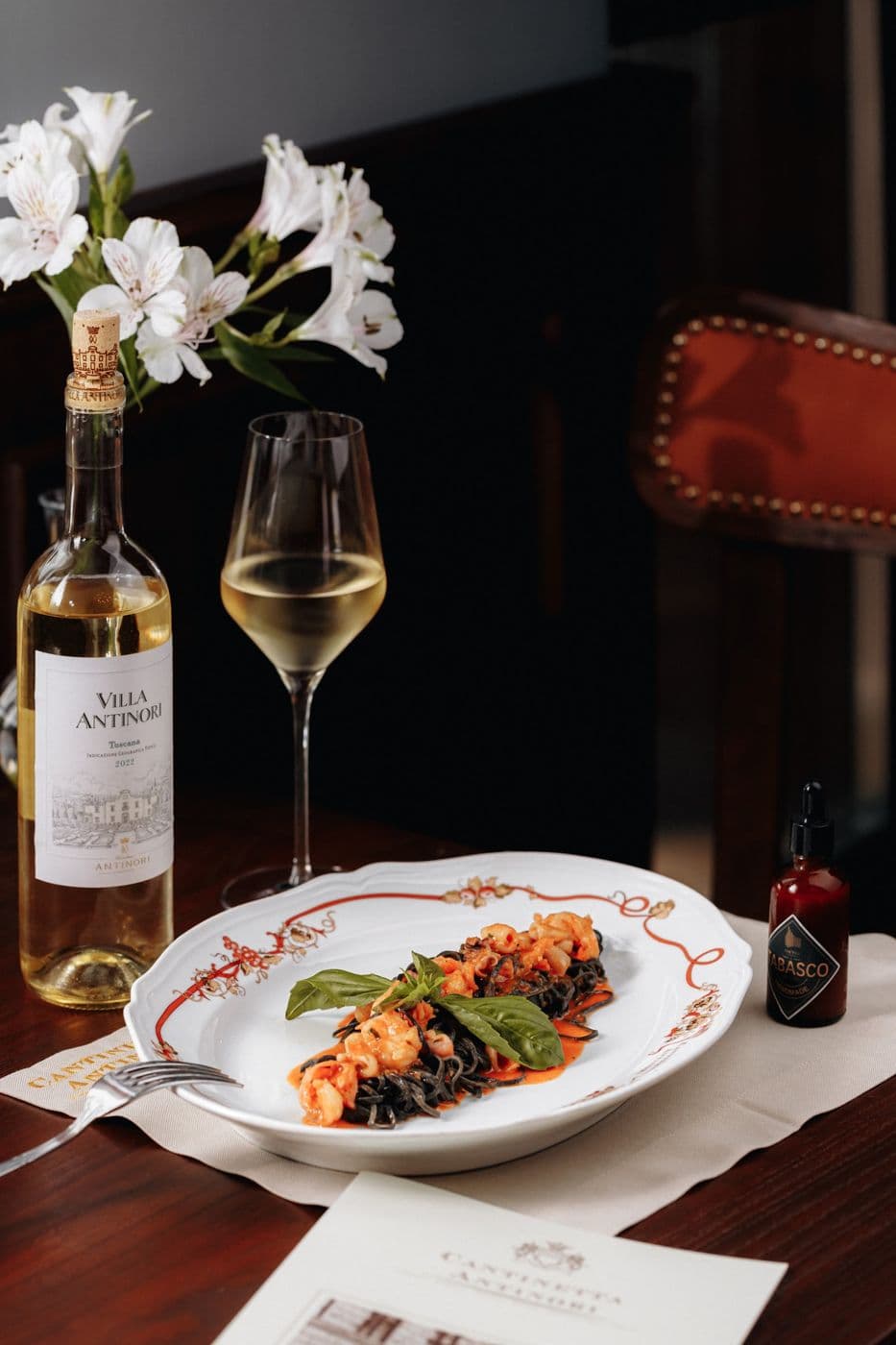 A dish with shrimp on a decorated plate with a bottle and a glass of white wine