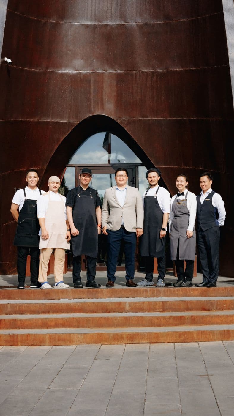A team of seven employees at the entrance of a building with a rust-brown façade