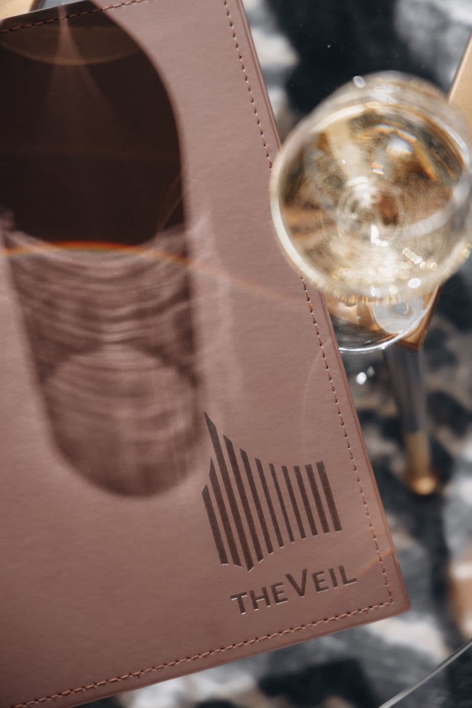 A leather menu with The Veil logo and a glass of sparkling wine