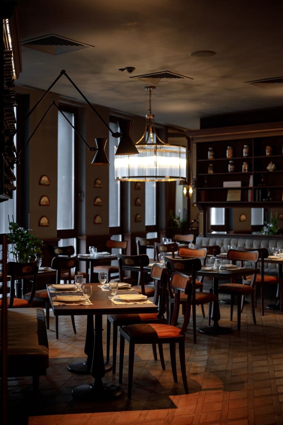 A restaurant hall with wooden furniture, a chandelier and laid tables